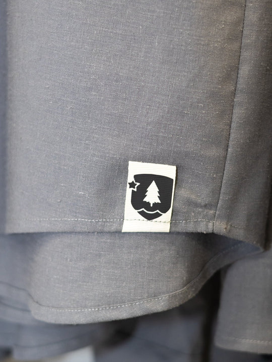 Close-up of a gray heathered fabric garment with a small white rectangular patch featuring a black tree and star logo.