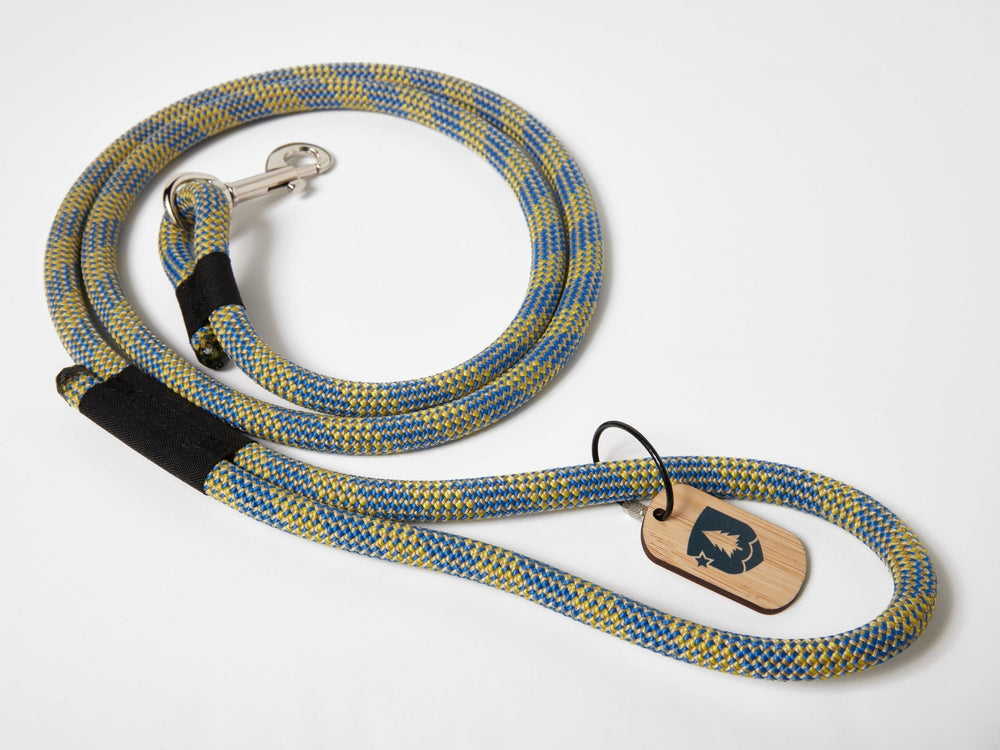 A dog leash made from upcycled climbing rope, featuring a metal clasp and a bamboo tag with a logo, laid out on a white surface.
